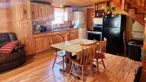 Un interior de madera con una mesa de comedor, sillas, un sofá, electrodomésticos de cocina y una escalera.