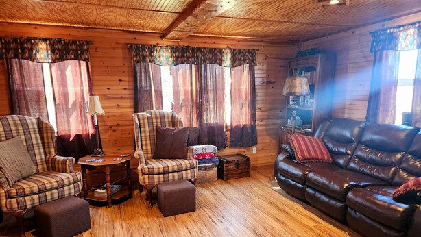 Un interior acogedor de cabaña de madera con un sillón escocés, un sofá de cuero y una mesa de centro de madera.