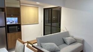 Un salon moderne avec un canapé gris, un meuble en bois contenant un four à micro-ondes et une fenêtre donnant sur la ville de nuit.