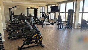 Une salle de sport équipée de machines de cardio, d’appareils de musculation et dotée d’une grande fenêtre laissant entrer la lumière naturelle.