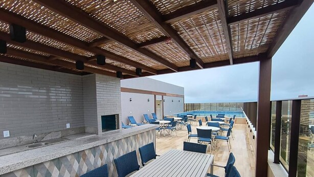 Un espace extérieur aménagé en terrasse, avec une longue table et des chaises, un bar doté d’un mur recouvert de carreaux, et une vue sur le paysage urbain grâce à de grandes fenêtres.