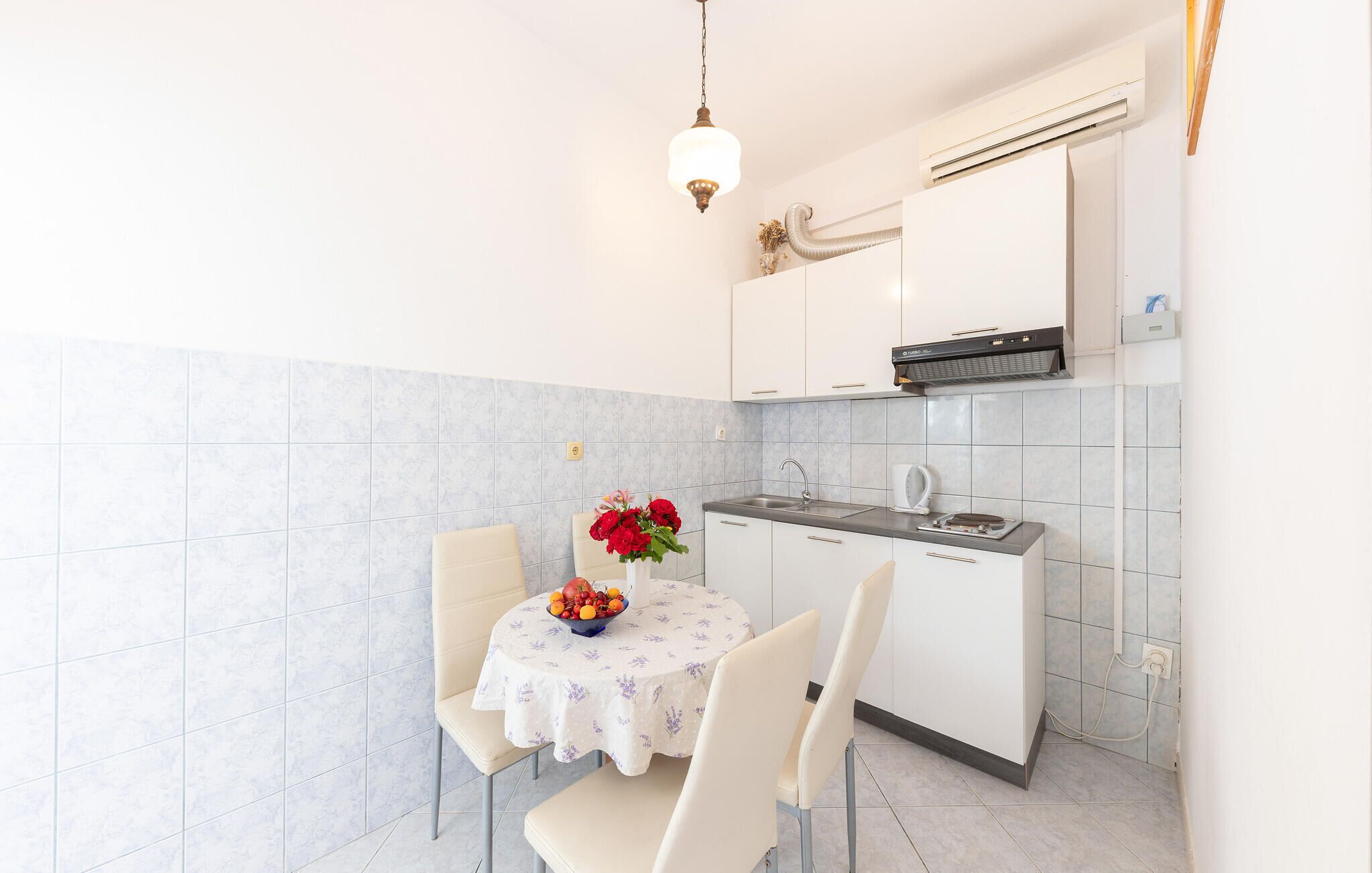 Una cucina compatta con pensili bianchi, piano cottura integrato e un piccolo spazio pranzo con tavolo e sedie.