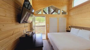 Ein Schlafzimmer in einer Holzhütte mit Bett, Wandfernseher und Balkon.