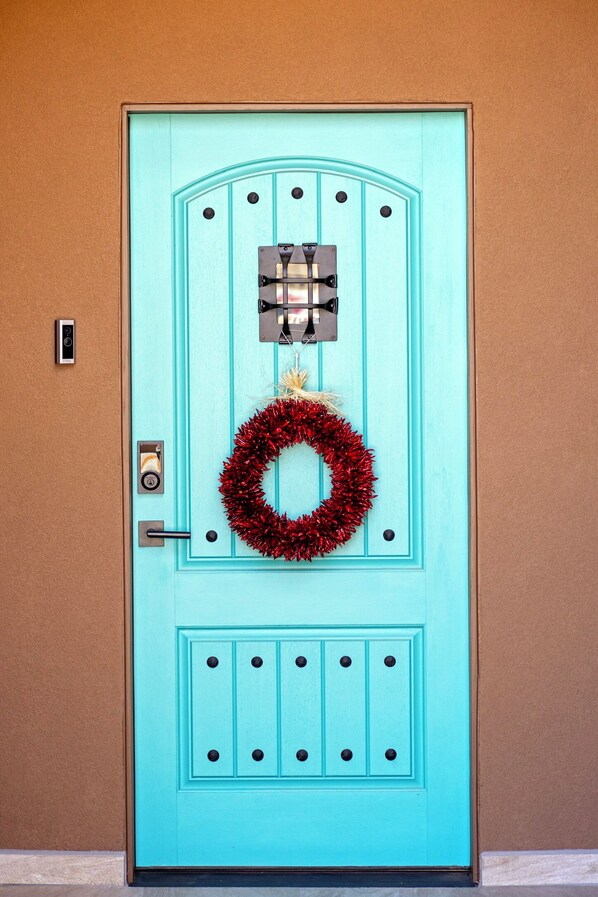 A turquoise door with a red wreath, a mail slot, and a doorbell.