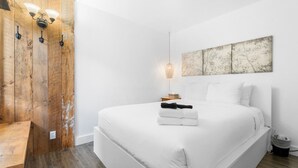 A bedroom with a large bed, a wooden wardrobe, a wall-mounted light fixture, and a painting.