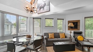 A modern living room with a glass dining table, grey sofa, and a chandelier.