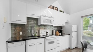 A modern kitchen with white cabinets, a black countertop, a microwave, a stove, and a refrigerator.