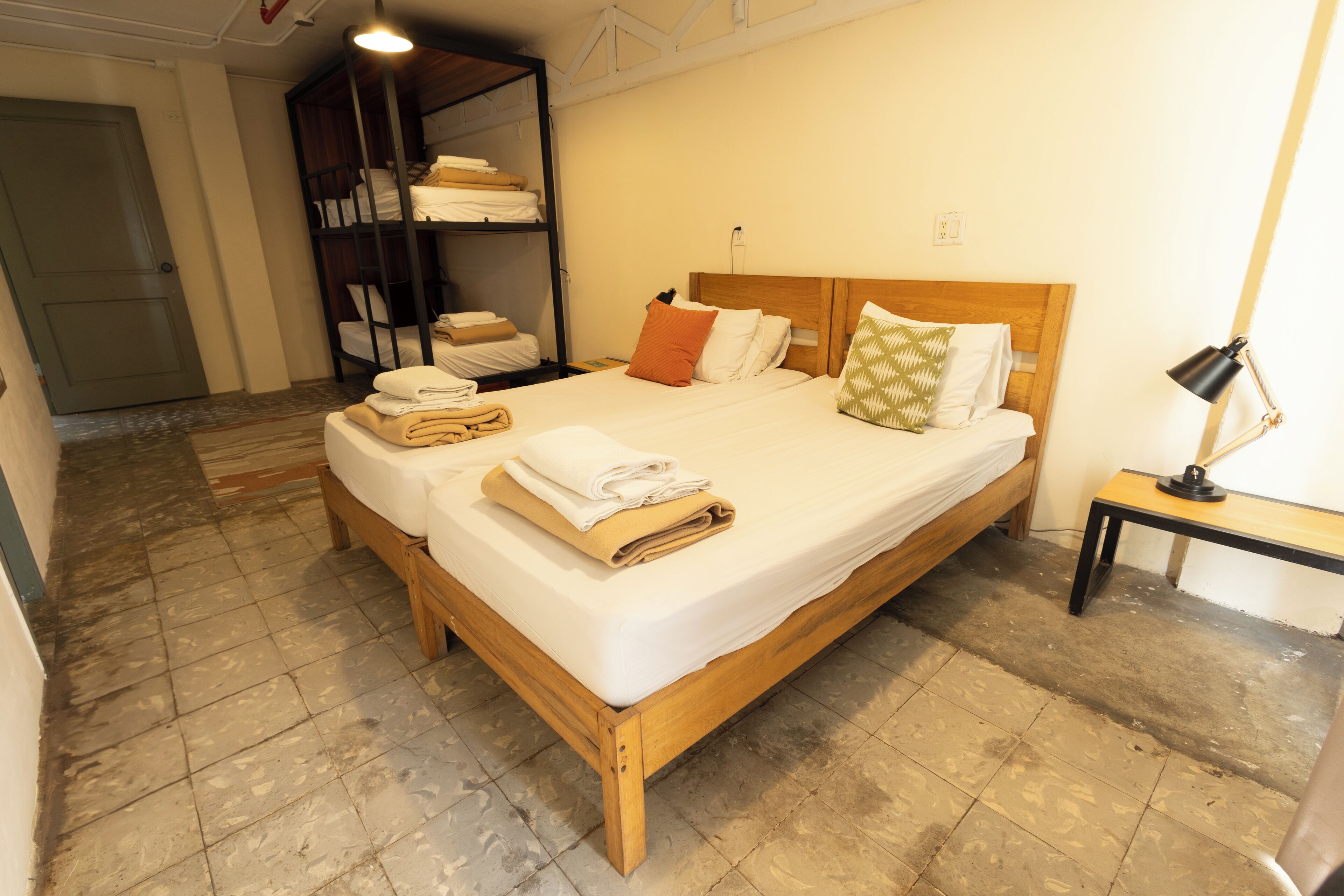 Een opgemaakt bed met gevouwen handdoeken, een houten hoofdbord en een nachtkastje met een lamp.