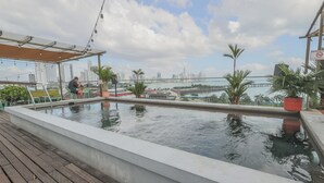 Una piscina en la azotea con vistas a la ciudad, plantas en macetas y una terraza de madera.