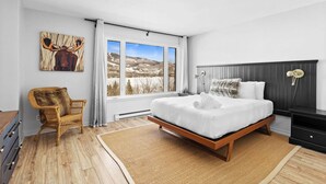 Un dormitorio con una cama grande, una silla, una mesita de noche y una ventana con vistas a la montaña.