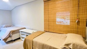 Une chambre avec deux lits, une armoire blanche et une fenêtre avec des stores.