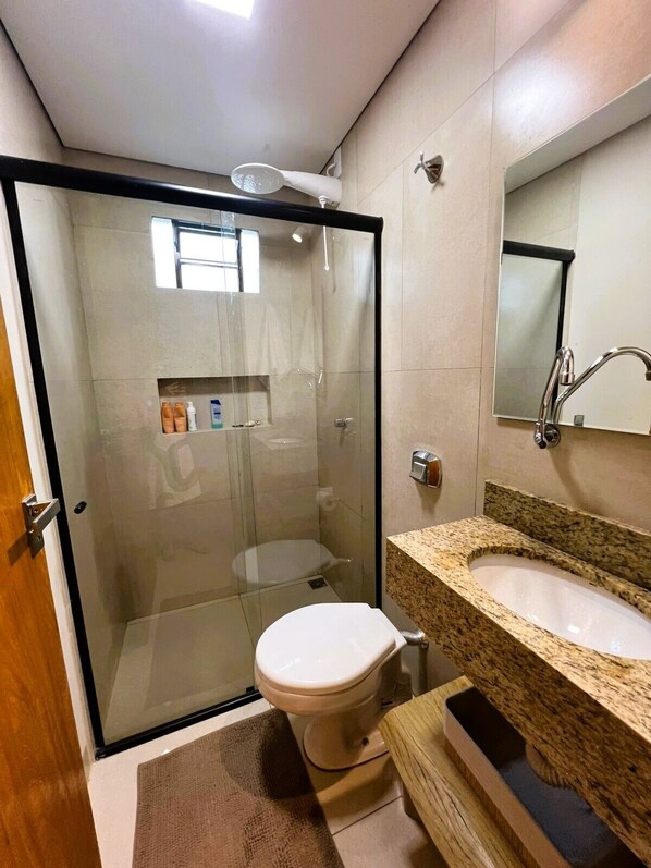A modern bathroom with a glass-enclosed shower, a toilet, a sink, and a mirror.