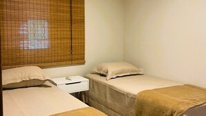 Une chambre avec deux lits simples, une table de chevet, une fenêtre avec stores et un appareil de climatisation.