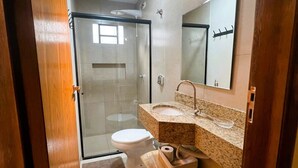 Une salle de bain moderne avec une douche à parois de verre, des toilettes, un lavabo doté d’un plan de travail en granit et un miroir.