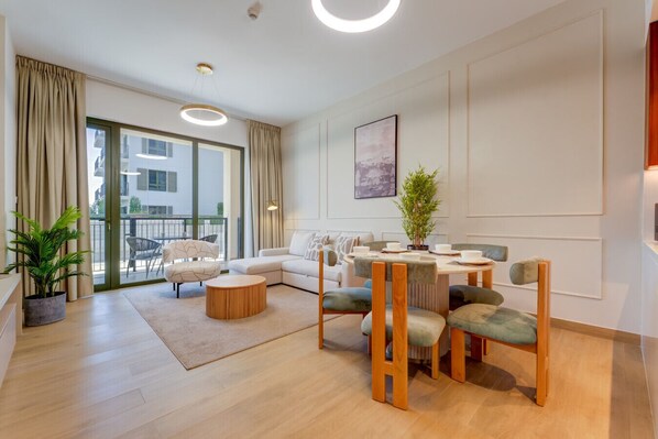 Un salon moderne avec un canapé, une table basse ronde et un ensemble de salle à manger. On y trouve une grande fenêtre avec des rideaux, une plante en pot et un tableau accroché au mur.