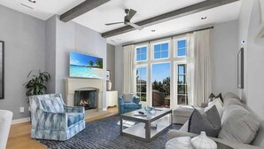 A modern living room with a fireplace, a ceiling fan, and a large window with curtains.