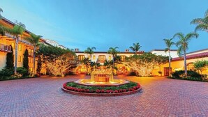 A courtyard with a central fountain, surrounded by palm trees and a brick pathway.