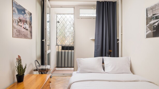 Un dormitorio con una cama, una mesita de noche de madera, una planta en maceta y una ventana con cortinas.