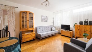 Una sala de estar con sofá, aparador de madera, televisor y una zona de comedor con mesa y sillas.