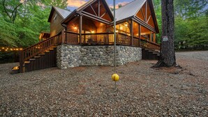 A log cabin with a stone foundation, wooden deck, and a stone wall.