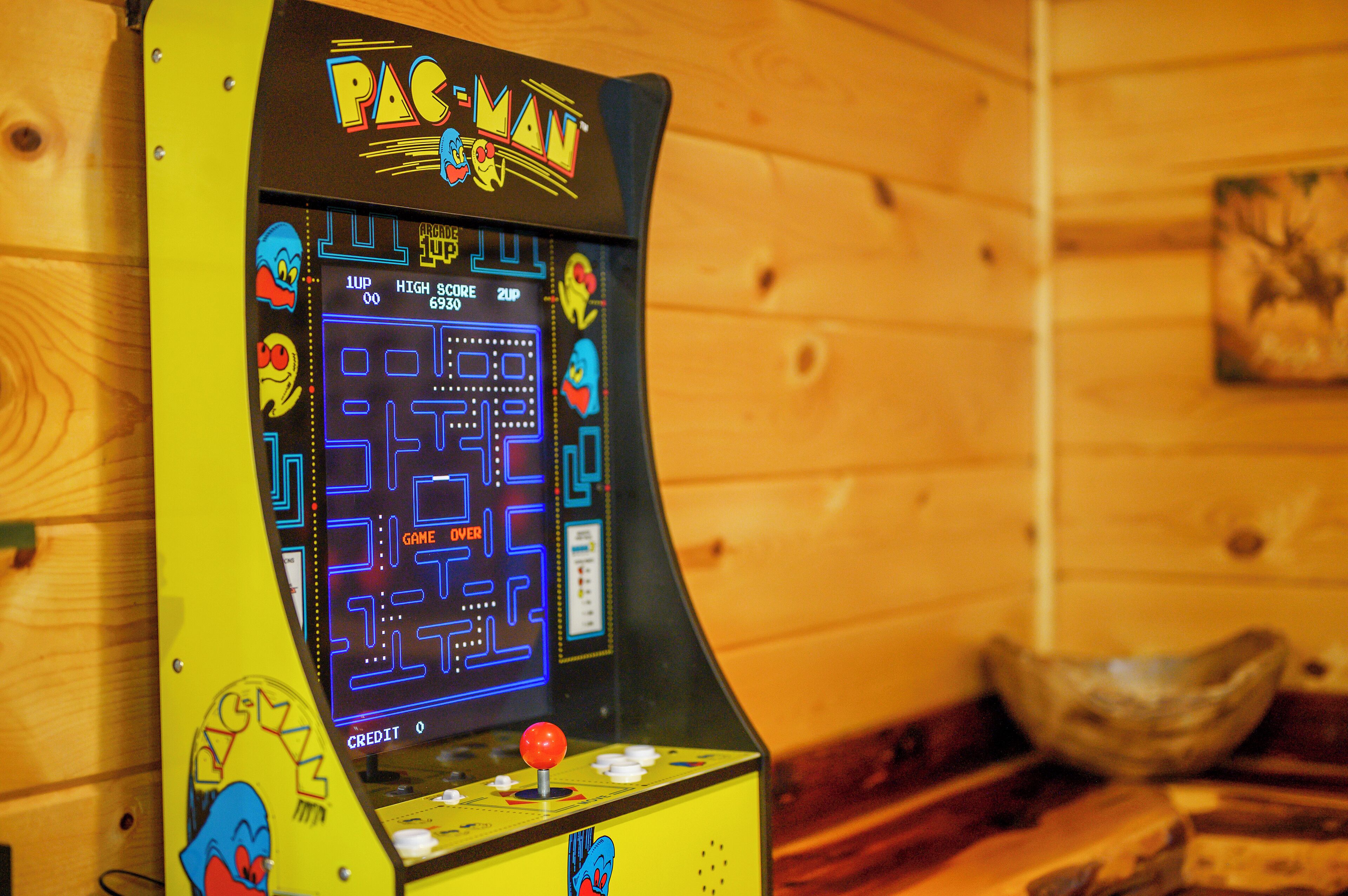 A Pac-Man arcade machine with a yellow and black design, set against a wooden wall.