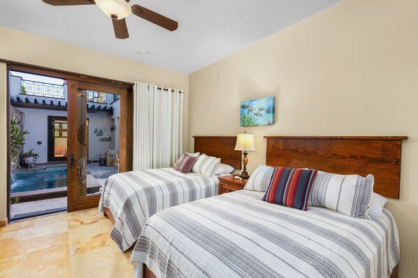 A hotel room with two beds, a wooden headboard, a painting, a lamp, and a view of an outdoor pool area.