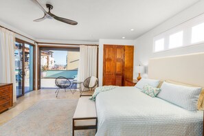 A bedroom with a bed, a ceiling fan, a wooden door, and a view of the outside.