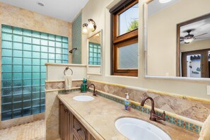A bathroom with two sinks, a large window with blue-tinted glass, and a ceiling fan.