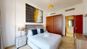 A hotel room with a large bed, a wooden wardrobe, a nightstand with a lamp, and a painting on the wall.
