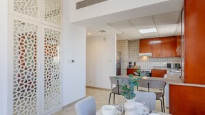 A modern kitchen with wooden cabinets, a dining area with a table set for four, and a decorative white partition with a geometric pattern.