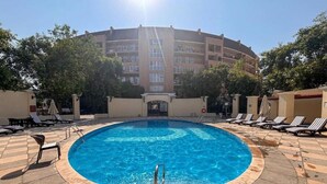 A circular pool with a metal ladder, surrounded by lounge chairs and a tiled deck.