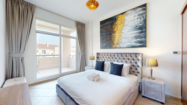 A hotel room with a large bed, a view of the city through a balcony, and a modern abstract painting on the wall.