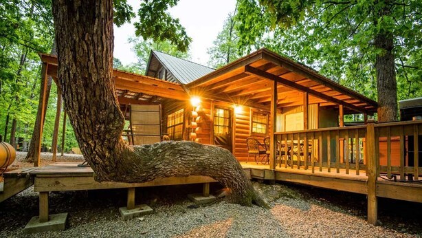 A rustic cabin with a wooden deck, large windows, and a covered porch area.