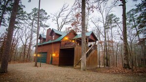 A log cabin with a green roof, a staircase leading to a deck, and a garage door. - Squirrel's Nest is a perfect two-bedroom hideaway with tree top views! (Broken Bow)