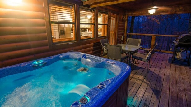A hot tub in a wooden cabin with a deck, outdoor seating, and a view of the forest. - Squirrel's Nest is a perfect two-bedroom hideaway with tree top views! (Broken Bow)