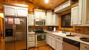 A kitchen with white cabinets, stainless steel appliances, and wooden flooring. - Squirrel's Nest is a perfect two-bedroom hideaway with tree top views! (Broken Bow)
