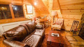 A cozy cabin interior with a leather sofa, a small round table, and a floral armchair. - Squirrel's Nest is a perfect two-bedroom hideaway with tree top views! (Broken Bow)