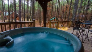 Ein Whirlpool auf einer Holzterrasse mit Blick auf einen Wald.