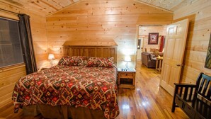 Ein Schlafzimmer in einer Holzhütte mit einem Bett, einem Nachttisch, einer Lampe und einer Tür zu einem anderen Raum.
