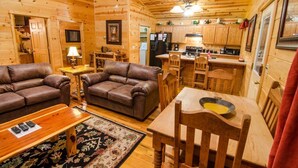 Ein gemütliches Blockhausschlafzimmer mit zwei Ledersofas, einem Holzespeisesaal und einer Küche mit Holzschränken und Geräten.