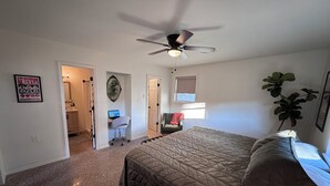 Ein Schlafzimmer mit einem Bett, einem Schreibtisch mit Computer, einem Deckenventilator und einer Pflanze.