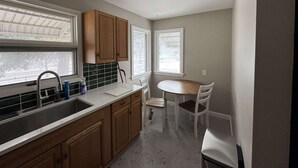 A kitchen with wooden cabinets, a white countertop, a sink, and a dining area with a table and chairs. - Newly remodeled 2-bedroom house with WiFi, conveniently located in Great Falls (Great Falls)