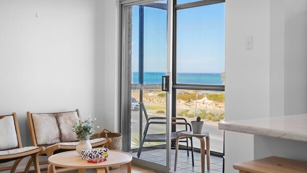 Un balcón con vista al mar, amueblado con sillas y una mesa, y una pequeña planta en maceta.