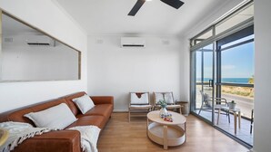 Un salón moderno con un sofá de cuero marrón, una mesa de centro redonda de madera y un amplio ventanal con vistas a la playa.
