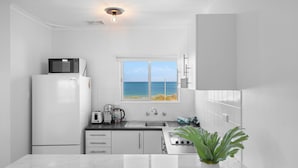 Cocina compacta con vistas al mar, incluye microondas, refrigerador, lavamanos y una planta.