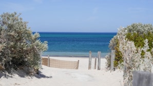 Una playa arenosa con un cerco de madera y vegetación escasa.