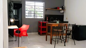 A compact kitchen with a dining area, a red chair, a wooden table, and a window with blinds. - Private, practical room for longer stays (Chetumal)