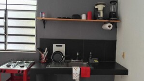 A kitchen with a gas stove, a sink, a coffee maker, and a shelf with kitchen items. - Private, practical room for longer stays (Chetumal)