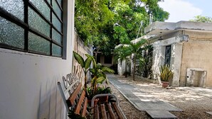 A pathway leading to a building with a bench, potted plants, and a wall with a metal gate. - Private, practical room for longer stays (Chetumal)