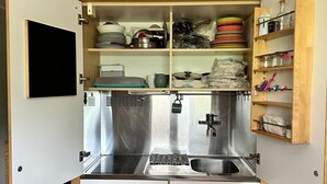 A compact kitchen with a stainless steel sink, two cabinets, and a wooden shelf unit above the sink. - Short periods Reggio Emilia center  (Reggio Emilia)